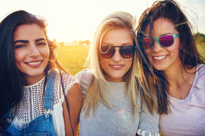 Close up of happy female friends sitting in sunny field with sun flare