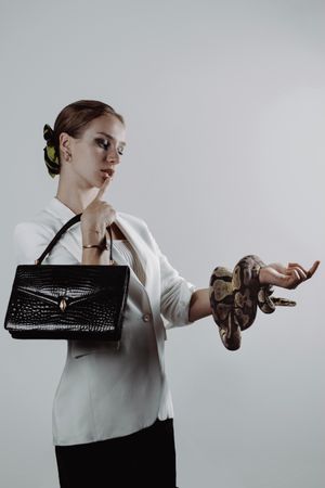 Woman holding dark leather bag with one hand and snake with the other hand