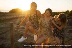 Happy women in summer dresses sitting on wooden fence at magic hour bGYYl5