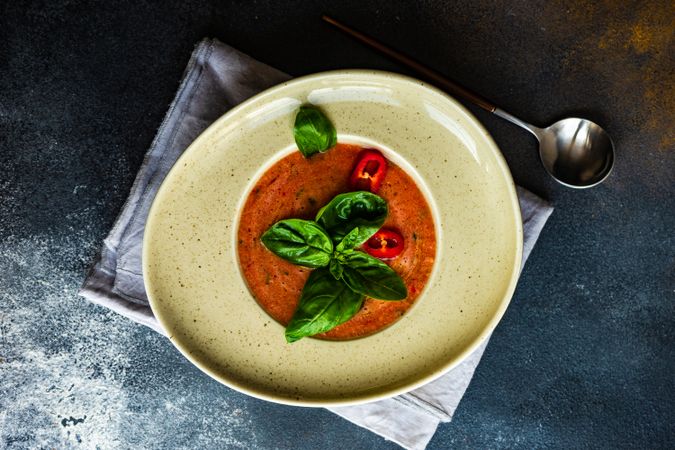 Top view of elegant ceramic bowl of gazpacho soup with basil leaves and pepper garnish with copy space