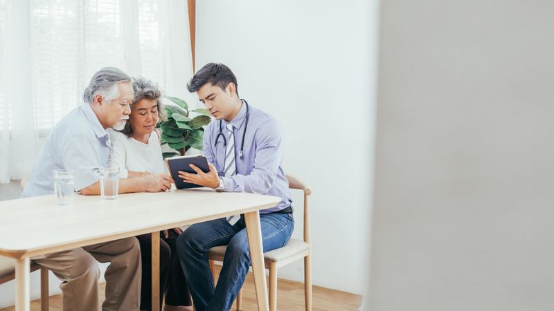 Doctor using digital tablet discussing test result and diagnosis with older couple