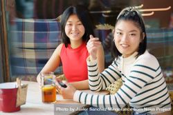 Two women sitting in restaurant patio with drinks looking at camera 4j2Pr4