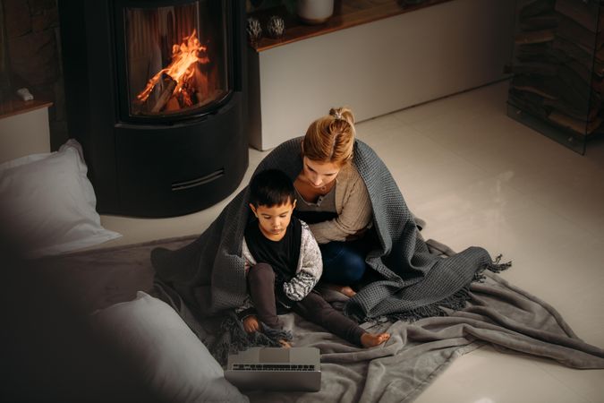 Top view of woman and a little boy with blanket sitting on floor looking at  laptop