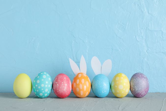 Decorated Easter eggs and cute bunny's ears on table against color background. Space for text