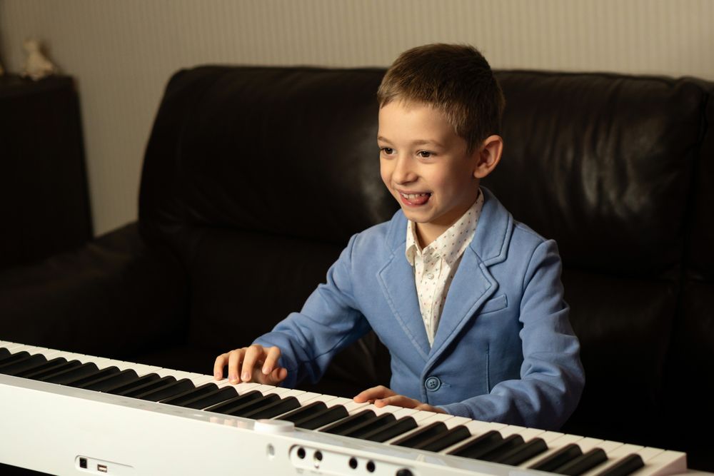 Cheerful young boy in blue blazer playing the piano.