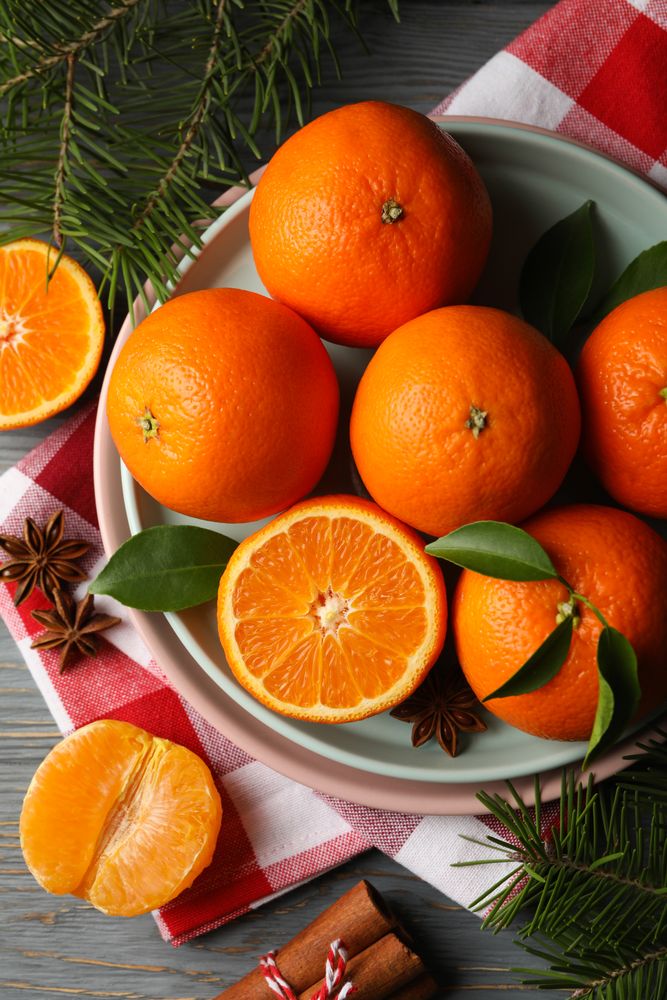 Plates with mandarins, pine branches, napkin and cinnamon on wooden background