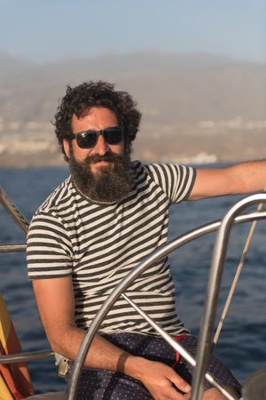 Smiling man holding steering wheel on yacht on water near quay