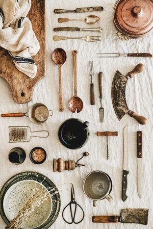 Vintage kitchen utensils and knifes artfully arranged on beige tablecloth with breadboard