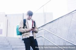 Young man walking down stairs with backpack while using mobile outdoors 4Zee7O