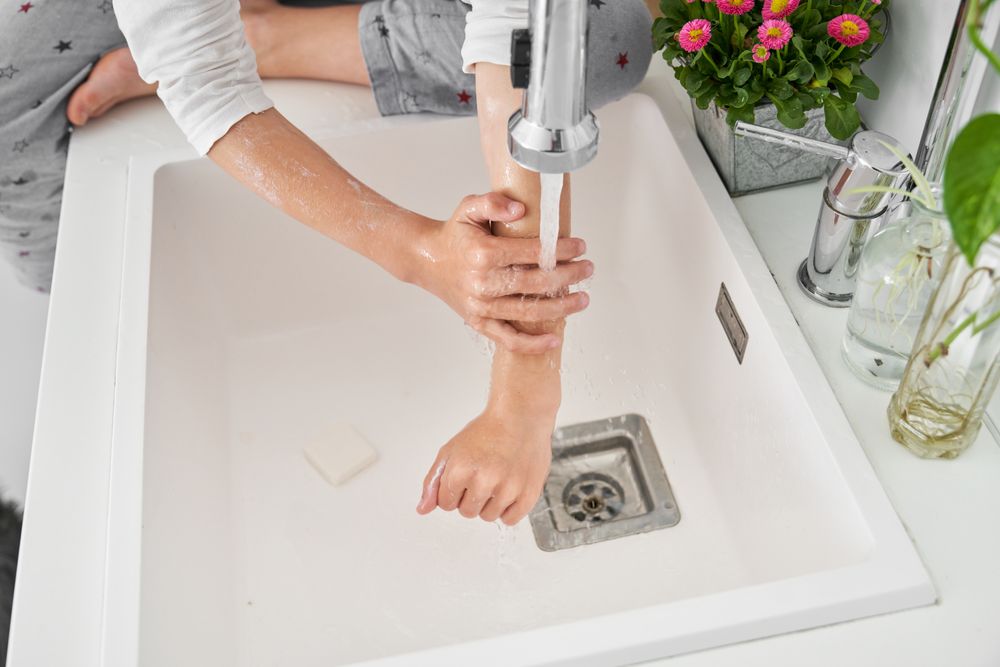 Faceless person cleaning hands in white sink