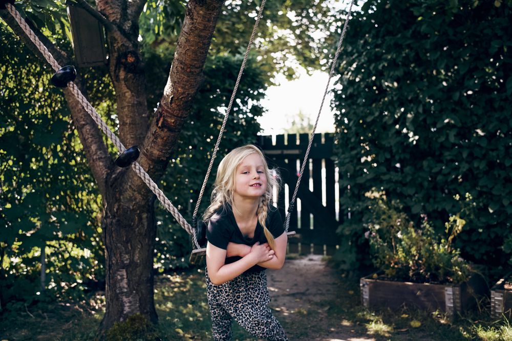 Blonde girl smiling with braided hair sitting on outdoor swing