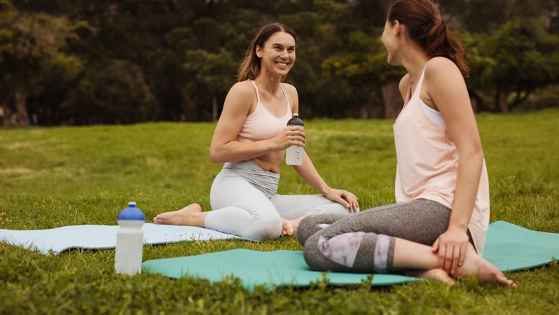 Fitness women sitting on yoga mats and relaxing during workout in a park