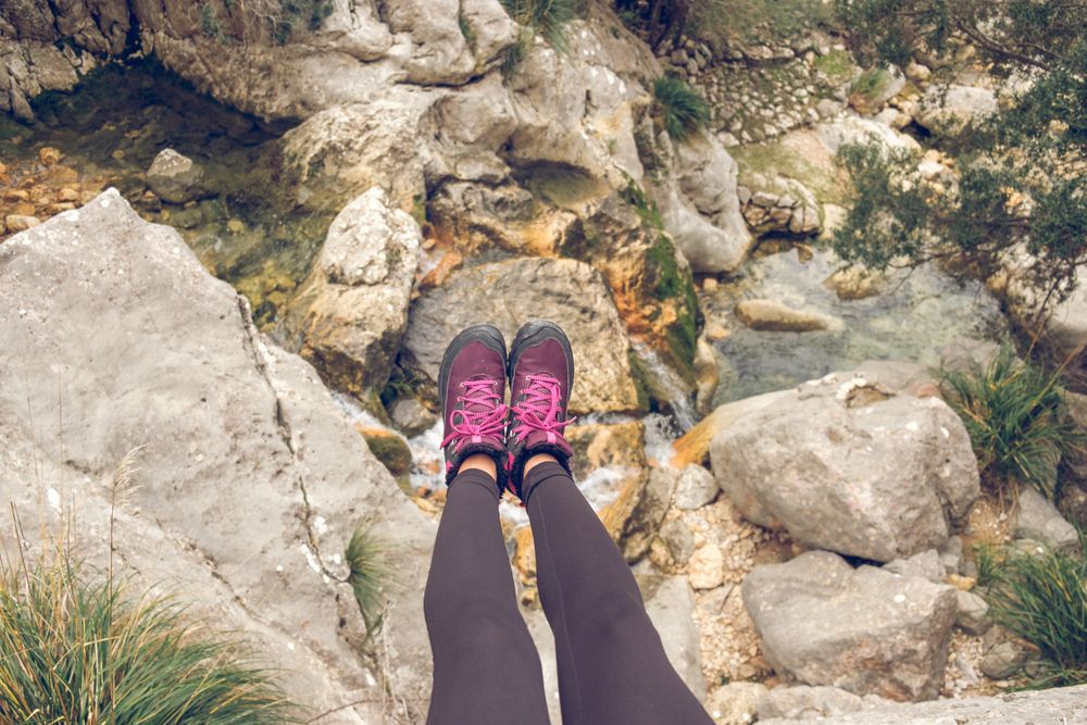 Crop female traveler sitting on rocky cliff with growing grass