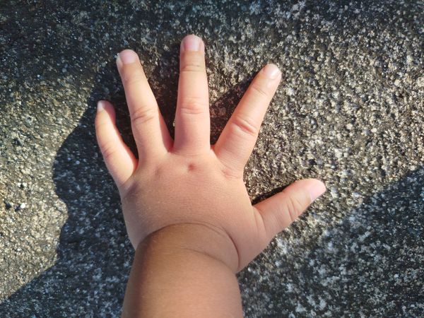 Baby Hand Reaching Toward Rough Concrete Surface