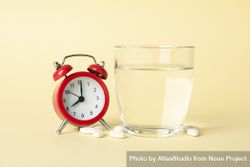 Glass of water with pills next to alarm clock in beige room 5ompkb