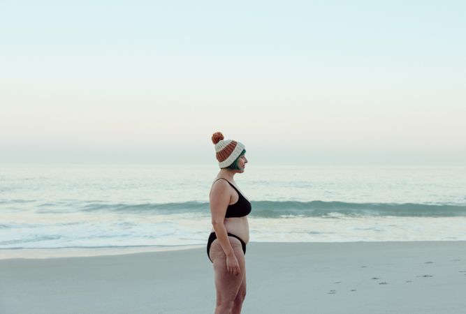 Sideview of a cheerful female winter bather standing at the beach in swimwear