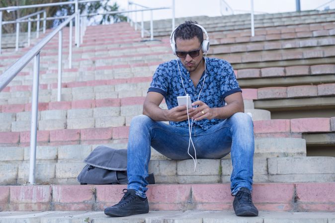 Man in jeans and blue shirt listening to music on smartphone