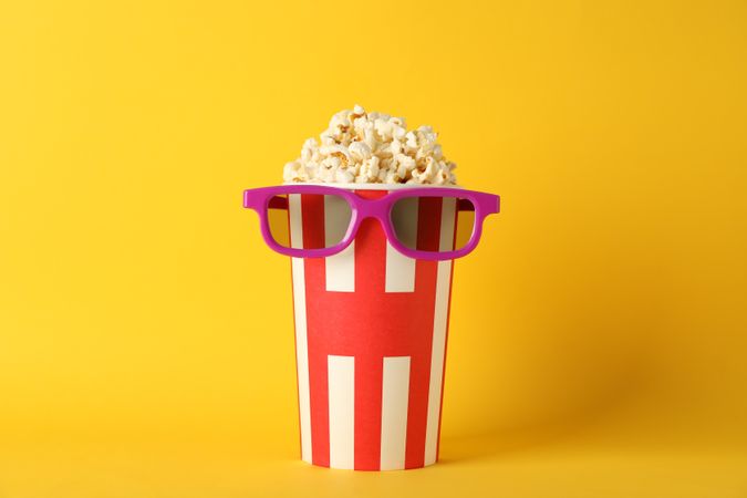 Striped bucket with popcorn and 3d glasses on yellow background, copy space