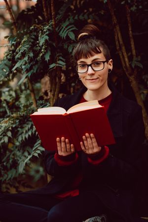 Young woman reading book on bench in park