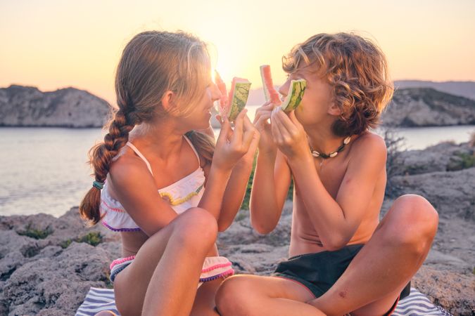 Happy brother and sister playing with watermelon rinds at seasid