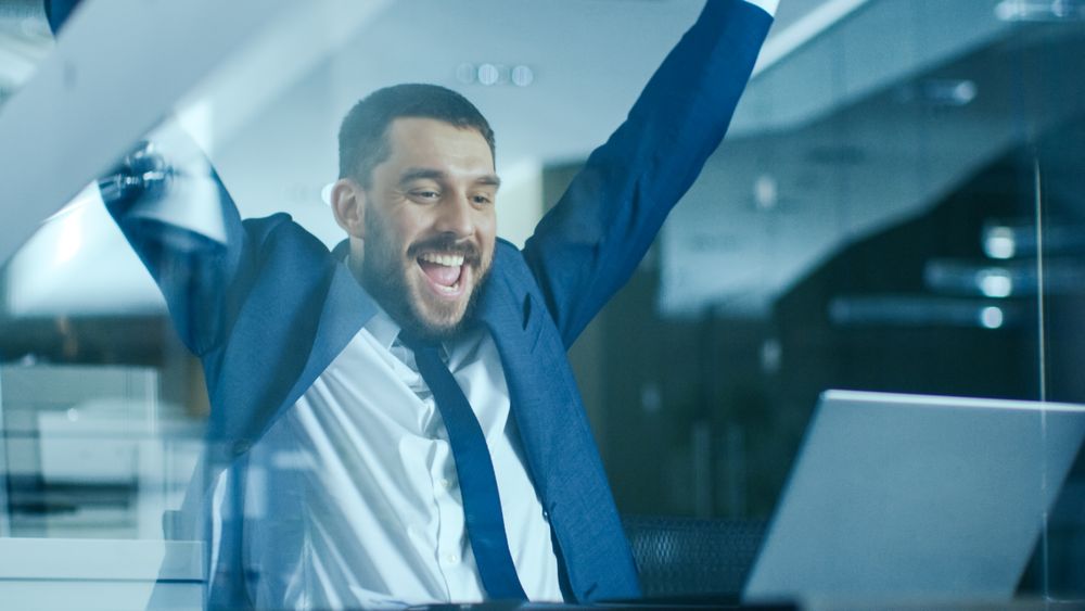 In the Office Businessman Sitting at the Desk Using Laptop Finishes Project and Wins Big.