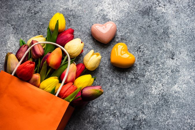 Ceramic pink and orange heart ornaments on grey counter with bag of fresh tulips