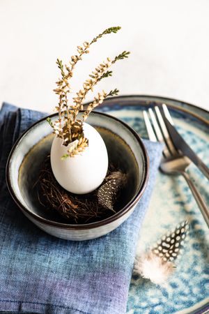 Easter table setting with decorative egg shell, feather and heather on blue plates