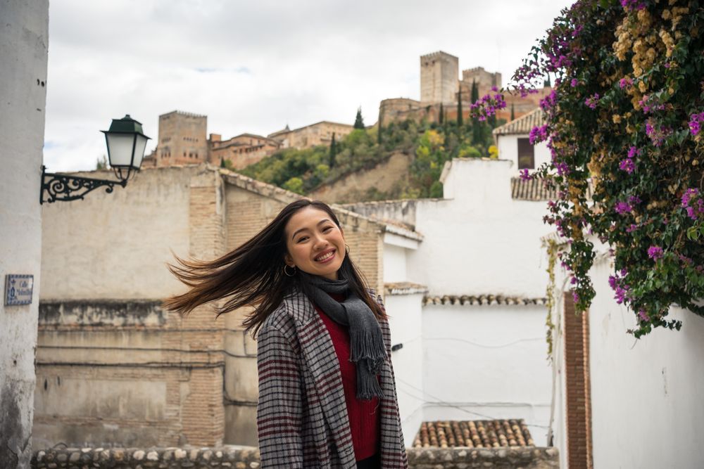 Asian female traveler in warm wear smiling among old buildings near big castle