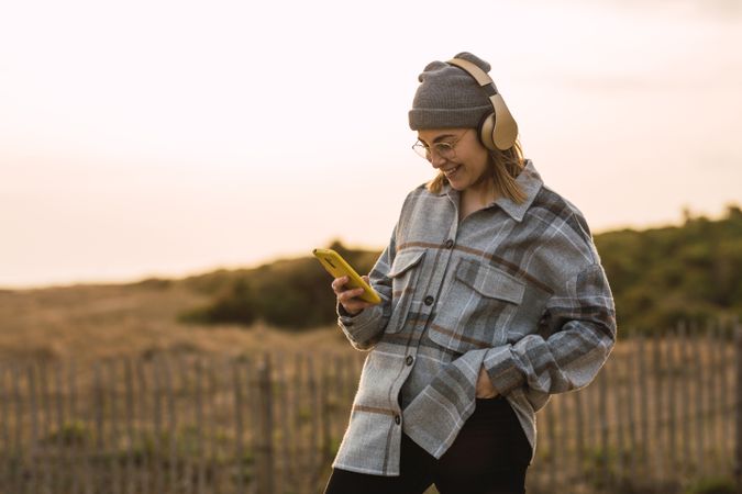 Happy young woman using smartphone and listening to music in headphones in countryside
