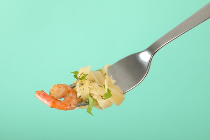 Fork with tasty pasta on mint background, close up