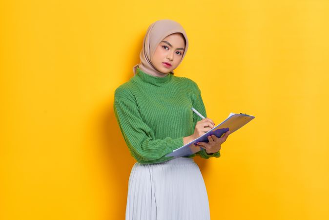 Woman in headscarf writing on clipboard in studio shoot