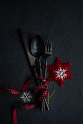 Dark knife and fork on dark background tied with festive red ribbon and snowflake ornament