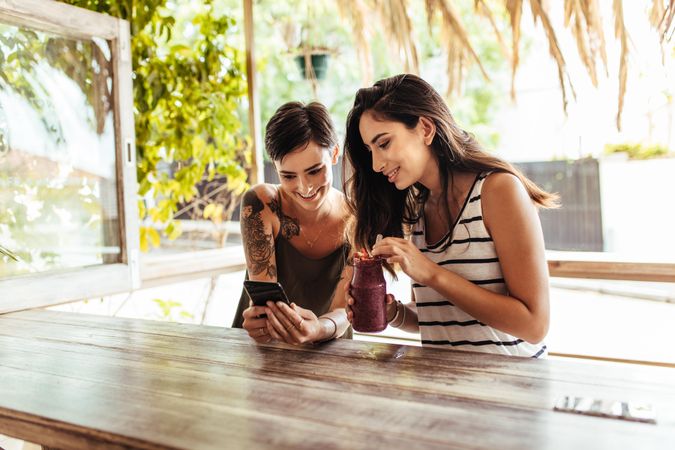 Two smiling women sitting at a restaurant looking at mobile phone