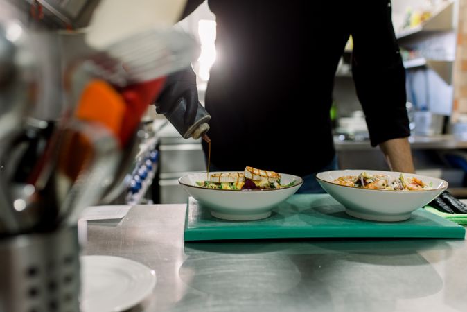 Crop anonymous male chef in uniform serving delicious salad with grilled cheese in kitchen of restaurant