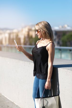 Side view of a blonde woman checking a smart phone on the street