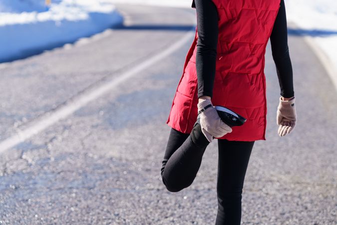 Cropped shot of fit woman in wintry gear stretching quadriceps in the mountains on cold day