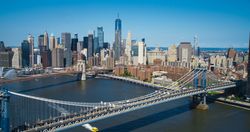 Iconic New York City Landscape Over East River with Skyscrapers, Manhattan and Brooklyn Bridges, Cars and Ferry Boats. Cinematic Urban Skyline with Clear Blue Sky