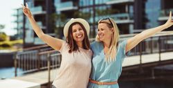 Women smiling and standing together with their arms up on sunny day