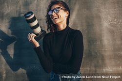 Woman photographer holding professional camera smiling against oliphant backdrop 0vydRb