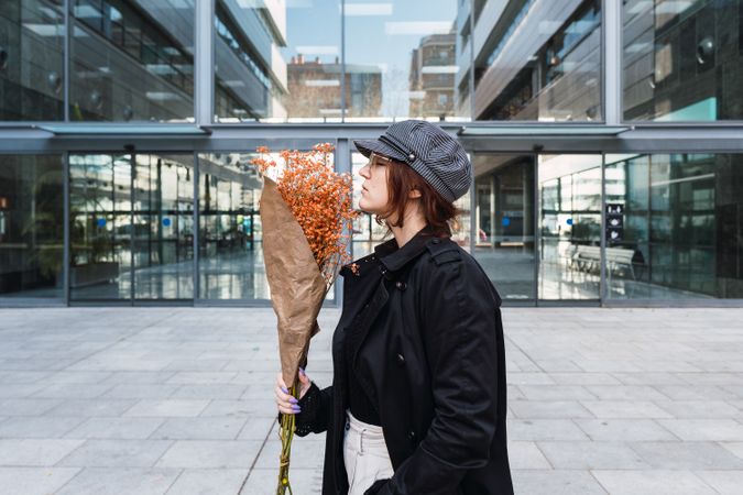 Stylish female smelling flowers on street