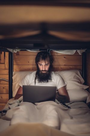 Man using laptop in rustic bunk bed