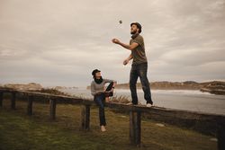 Man juggling balls on bench near woman with drum on shore