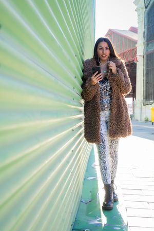 Trendy woman with smartphone near wall