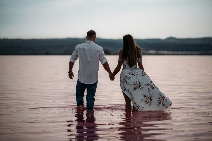 back view of adorable couple walking into an amazing beach with pink water