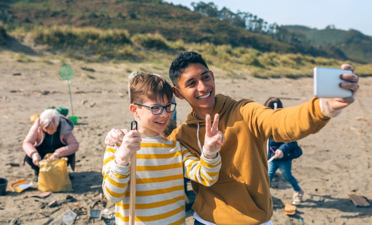 Young man and boy taking selfie to group of volunteers cleaning beach