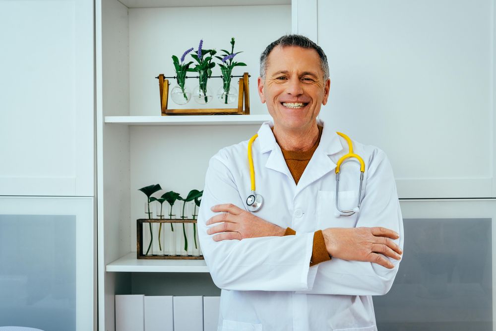 Confident mature doctor standing in office with arms crossed and smiling
