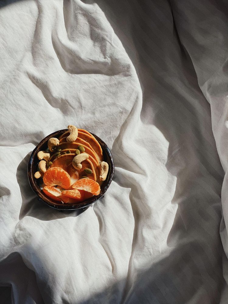 Top view of breakfast bowl of fresh orange slices, nuts and mini pancakes in morning light