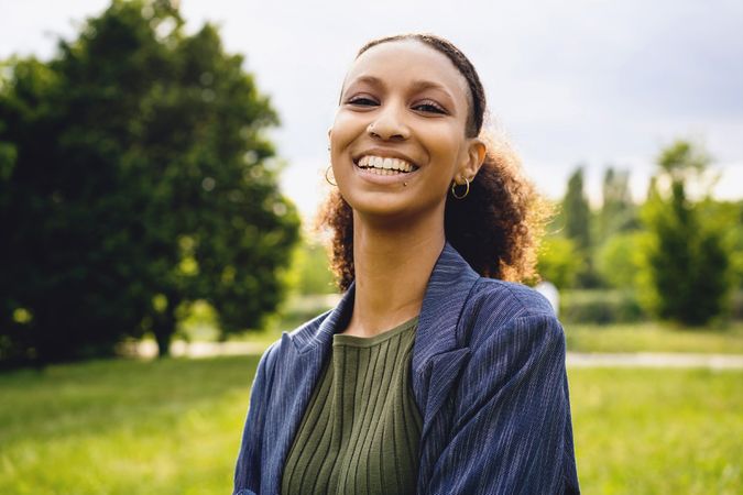 Genuine outdoor portrait of a Black woman with nose and lip piercing and curly hair tied into a ponytail