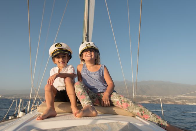 Smiling children sitting on deck of yacht in sea
