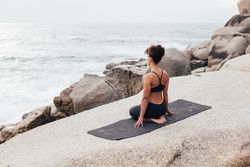 Female sitting next to the ocean sitting on knees gazing at the waves